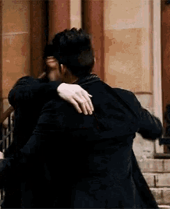 two men are hugging each other while standing in front of a building .