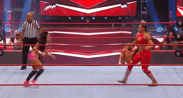 two women are wrestling in a wrestling ring with a referee watching .