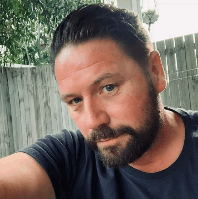 a man with a beard wearing a black shirt looks at the camera