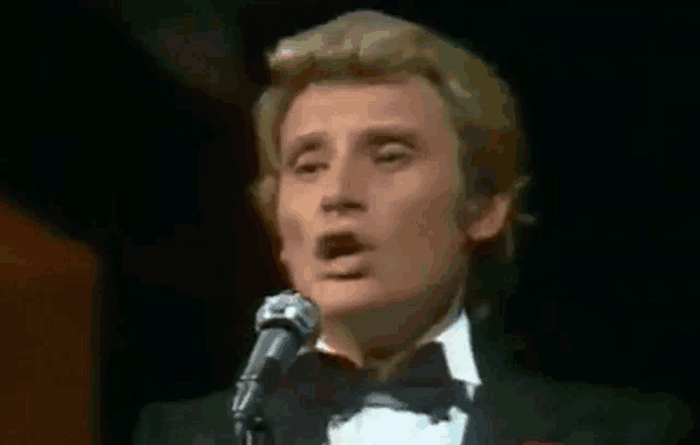 a man in a tuxedo and bow tie is singing into a microphone on a stage .