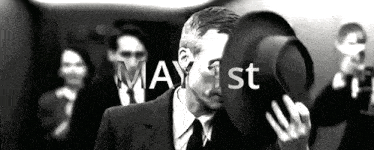 a man in a suit and tie is holding a hat in front of his face and the date may 1st is written above him