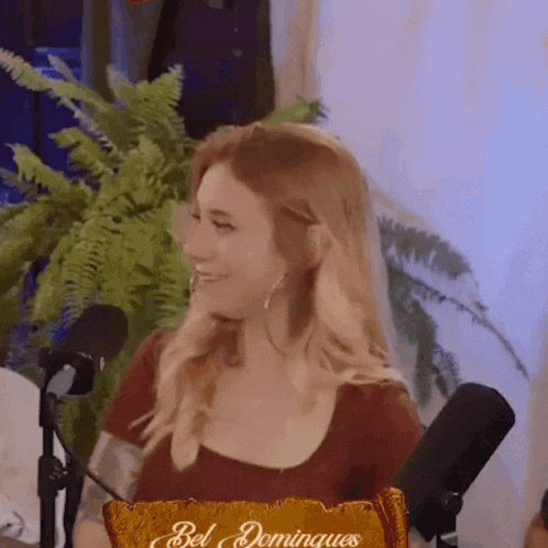 a woman sitting in front of a microphone with the name bel domingues on a sign