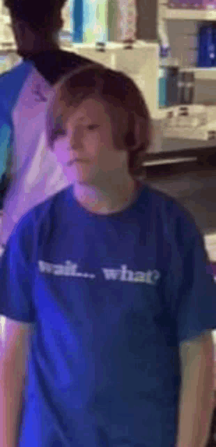 a boy wearing a blue t-shirt that says `` wait what '' is standing in a store .