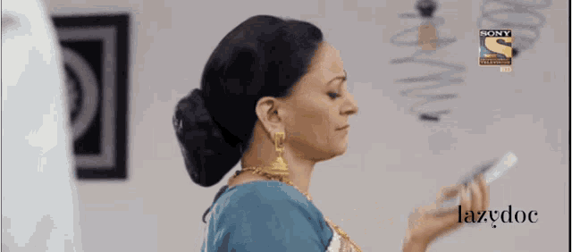 a woman in a blue dress is holding a cell phone in front of a sony logo .