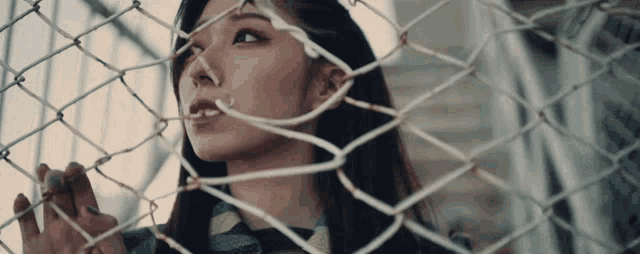 a woman is behind a chain link fence looking through it