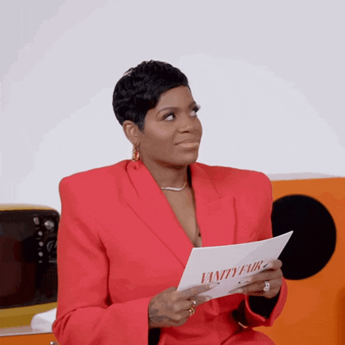 a woman in a red suit is holding a piece of paper that says vanity fair on it