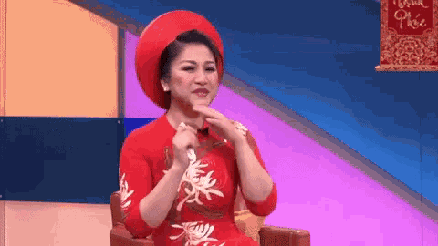 a woman in a red dress and red hat is sitting in a chair holding a microphone .