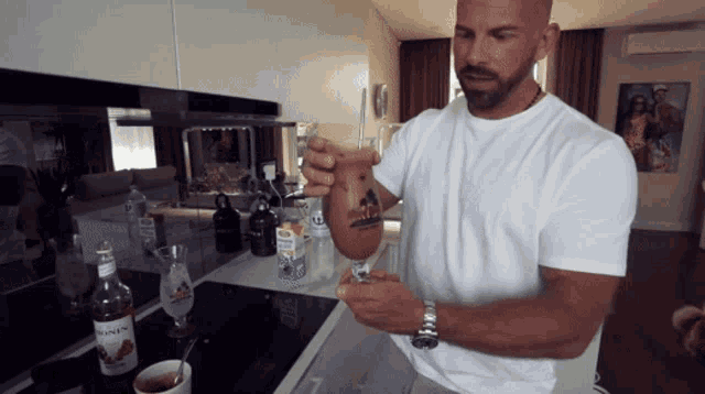 a man in a white shirt is pouring a drink from a glass