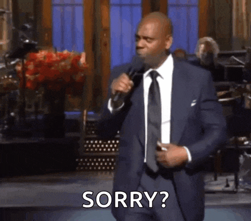 a man in a suit and tie is standing in front of a microphone and says sorry .
