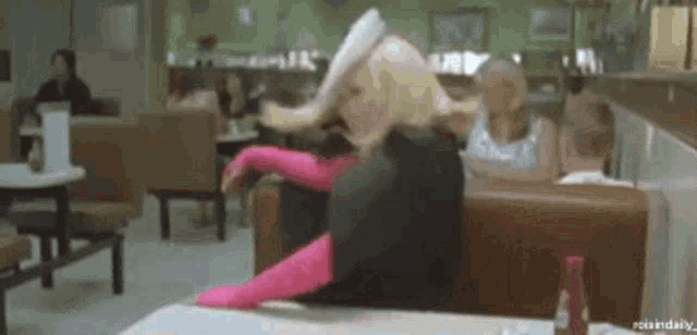 a barbie doll is sitting at a table in a diner with her legs crossed .