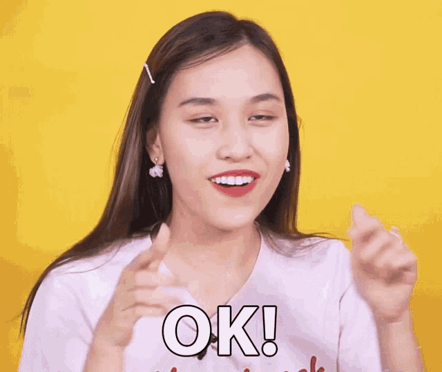a woman is clapping her hands in front of a yellow background and the word ok is on her shirt
