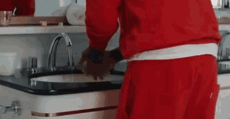 a man in a red sweater is washing his hands in a bathroom sink .
