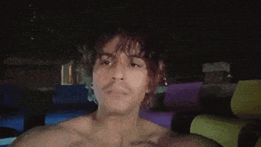 a man without a shirt is taking a picture of himself in a pool at night .
