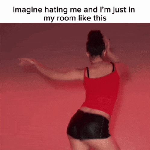a woman in a red tank top and black shorts is dancing in front of a red wall ..