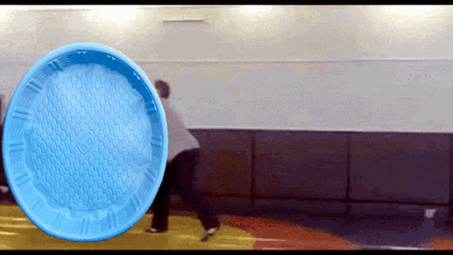 a blue frisbee is being thrown by a person in a gym