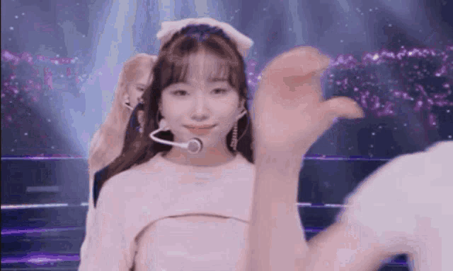 a group of girls are dancing on a stage and one of them is wearing a headband with a bow on it .