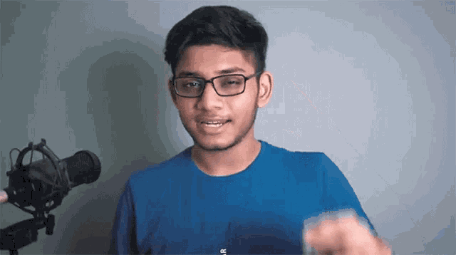 a young man wearing glasses and a blue shirt is standing in front of a microphone ..