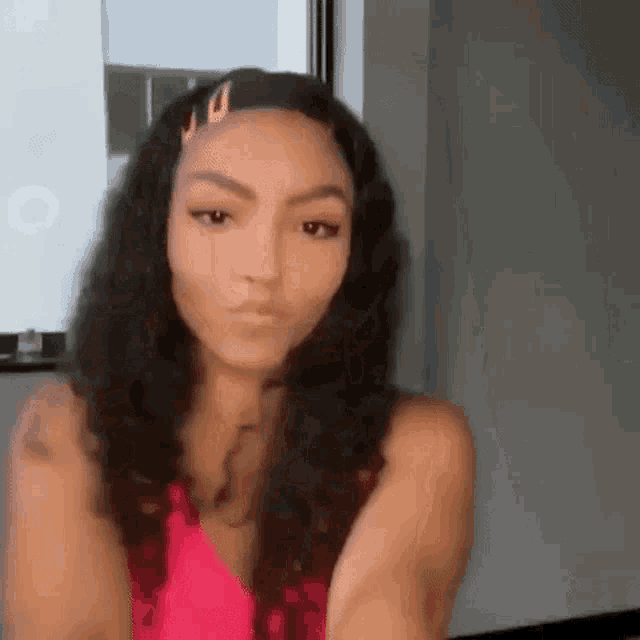a woman with long curly hair is wearing a pink tank top .
