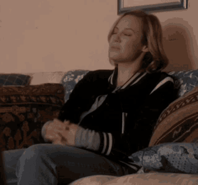 a woman in a black jacket sits on a couch