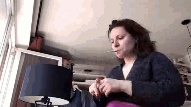 a woman is smoking a cigarette in front of a lamp in a room .