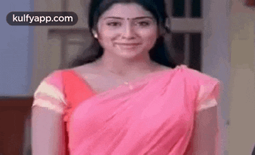 a woman in a pink saree is smiling while standing in front of a window .