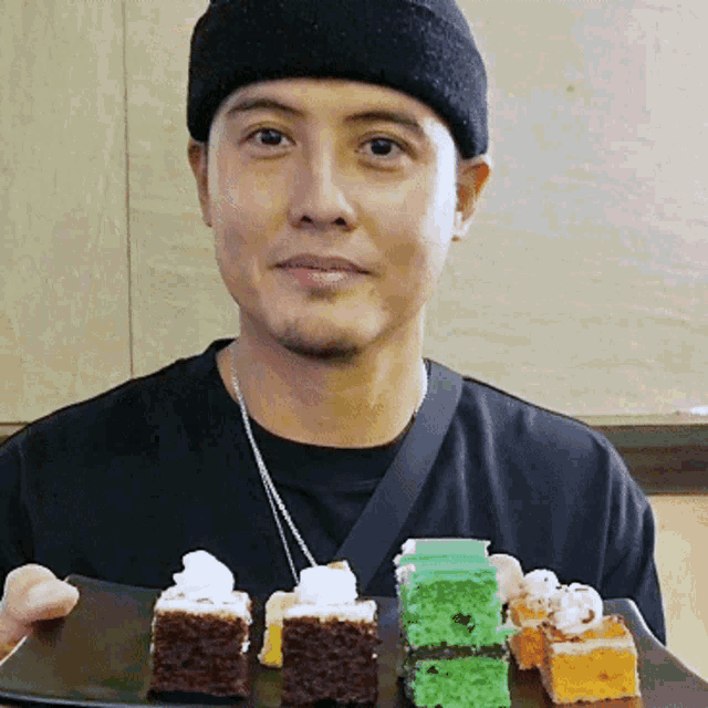a man in a black hat is holding a tray of cakes
