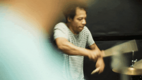 a man in a striped shirt is playing drums with a wooden stick