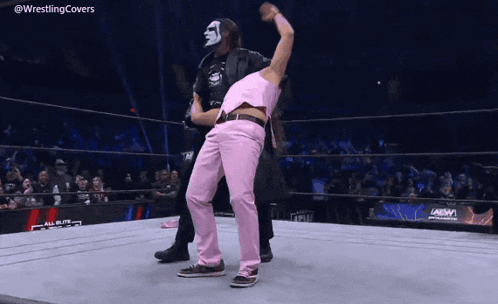 a man in pink pants is standing on a wrestling ring next to another man