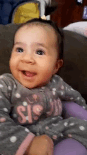 a baby is smiling while sitting on a couch and wearing a polka dot shirt .