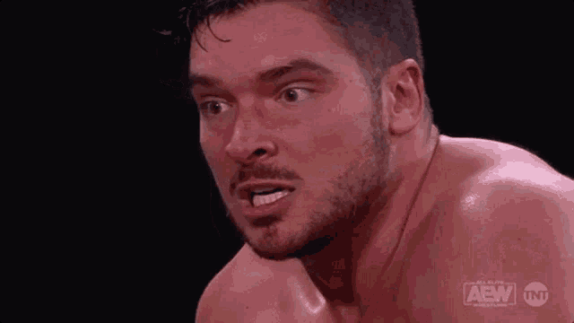 a shirtless wrestler with a beard is making a funny face in a wrestling match .