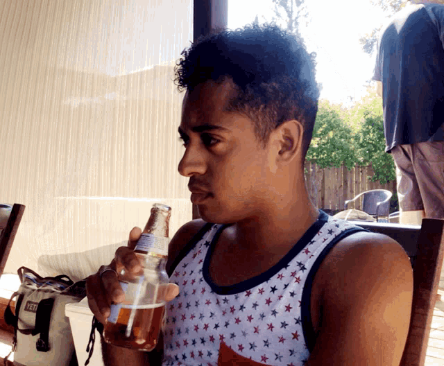 a man wearing a tank top with stars is drinking from a bottle
