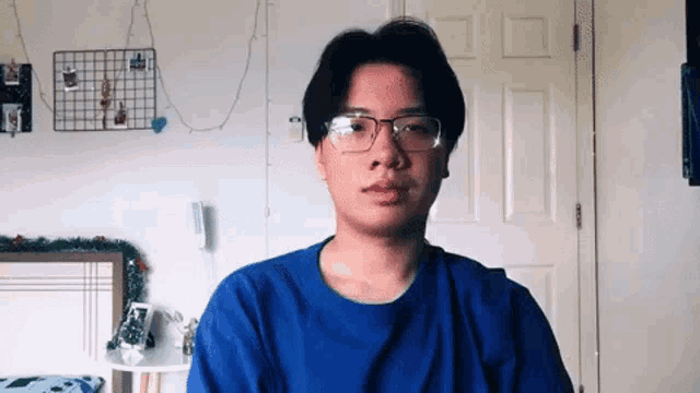 a man wearing glasses and a blue shirt is standing in front of a door .