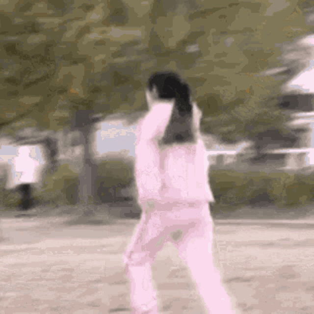 a girl in a pink tracksuit is standing in a park .