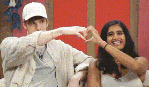 a man and a woman are making a heart shape with their hands while sitting next to each other .