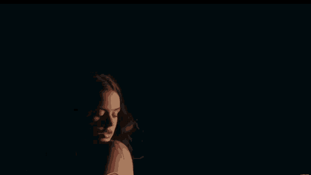 a woman is standing in the dark with her hair blowing in the wind