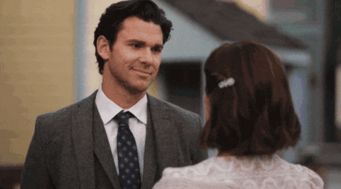 a man in a suit and tie is smiling at a woman in a white dress