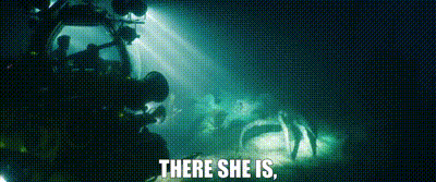 a man is taking a picture of a group of people in a dark room with the words `` there she is '' .