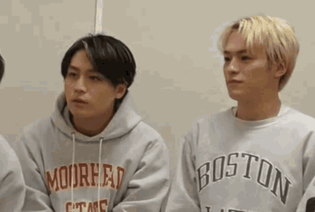 two young men are sitting next to each other wearing sweatshirts with boston on them .