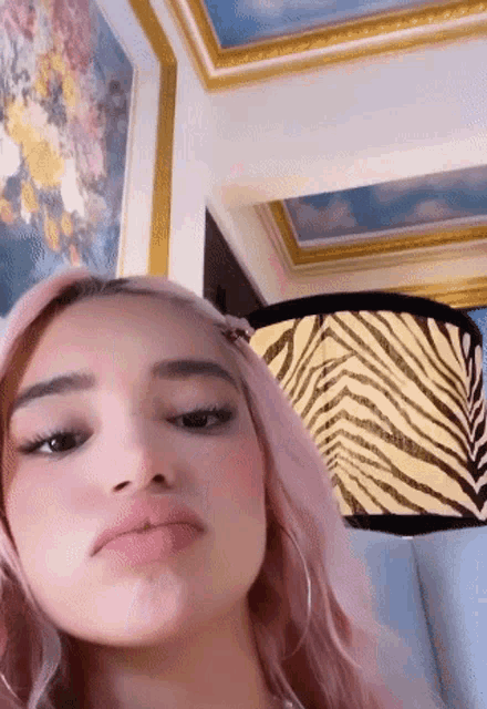 a woman with pink hair is making a face in front of a lamp with a zebra print on it .