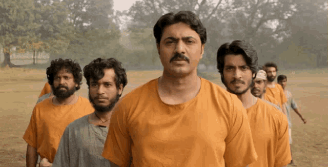 a group of men are standing in a line wearing orange shirts