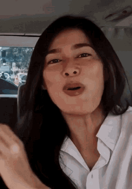 a woman in a white shirt is sitting in the back seat of a car making a funny face .