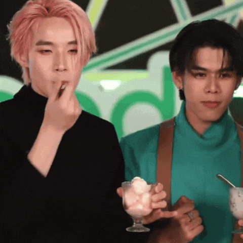 a man with pink hair is eating ice cream next to another man holding a glass of ice cream .