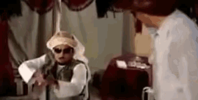 a man wearing sunglasses and a turban is standing next to another man in a room .