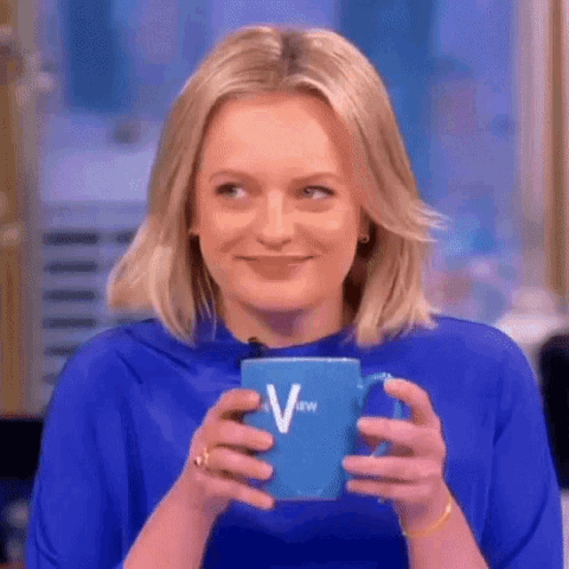a woman in a blue shirt is holding a blue coffee mug with the letter v on it .