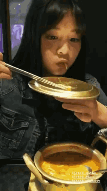 a girl is eating a bowl of soup with chopsticks and a pot of soup