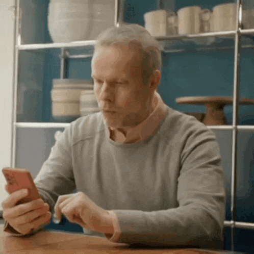 a man is sitting at a table looking at his cell phone .
