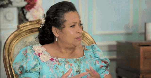a woman wearing a blue floral dress is sitting in a chair