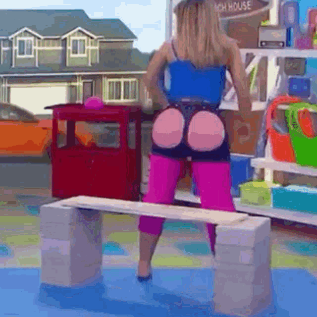 a woman in a blue tank top and pink pants is standing on a bench