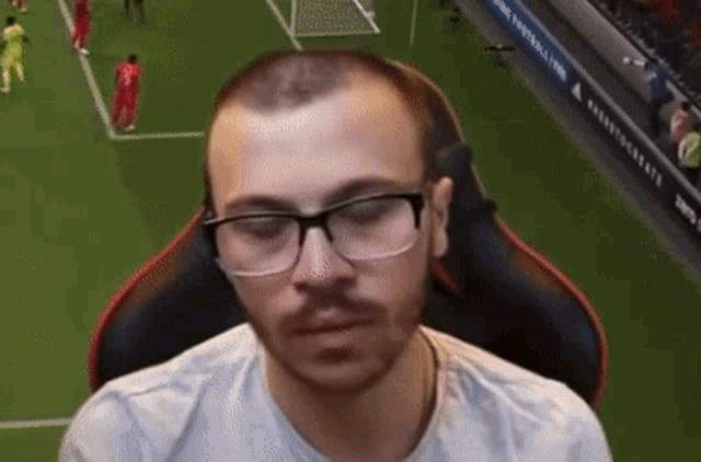 a man wearing glasses sits on a soccer field