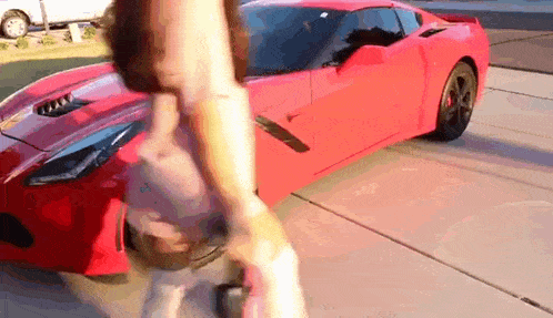 a woman is walking past a red sports car